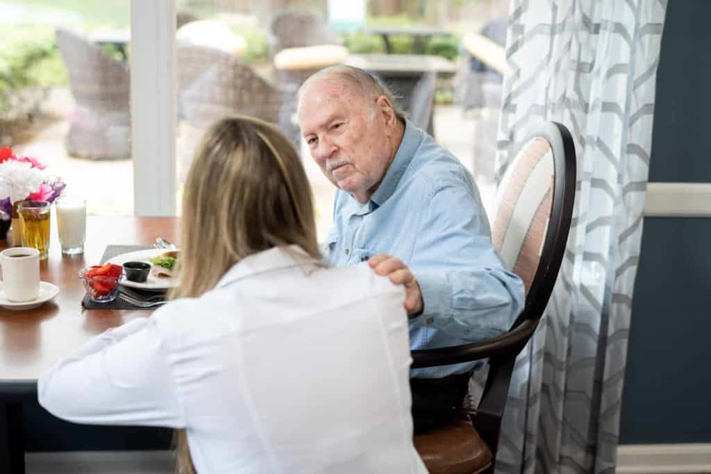 Staff member kneeling besides a seated senior man